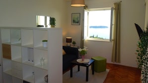 Un salon comprenant un canapé, une table basse, une lampe, une fenêtre donnant sur la mer et une étagère décorative.