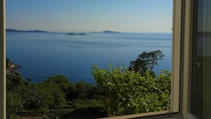 Une vue à travers une fenêtre sur un paysage côtier, avec une mer calme et des îles lointaines.