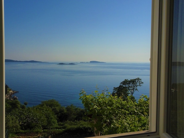 Vista a través de una ventana de un paisaje costero con mar tranquilo y islas distantes.