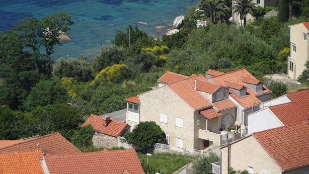 Un quartier résidentiel en bord de mer, avec des maisons aux toits de tuiles rouges, une végétation luxuriante et une vue dégagée sur la mer.