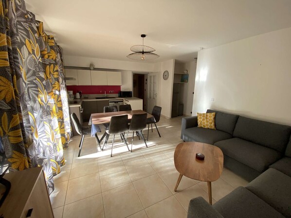 A modern living room with a grey sofa, a wooden coffee table, and a dining area with a wooden table and chairs. - Sanary , CLIM , beaches and shops , terrace and communal garden. (SANARY SUR MER)
