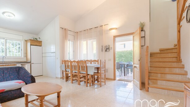 Un grand espace de vie comprenant une table et des chaises de salle à manger, un canapé, une cuisine équipée d’un réfrigérateur et un escalier.