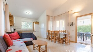 Un grand espace de vie comprenant un canapé, une table à manger et des chaises. On aperçoit une cuisine au fond.