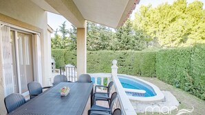 Une terrasse extérieure avec une table et des chaises, une piscine et une haie bien entretenue.