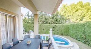 Eine Außenpatio mit Esstisch und Stühlen, einem Schwimmbecken und einem gepflegten Hecken.