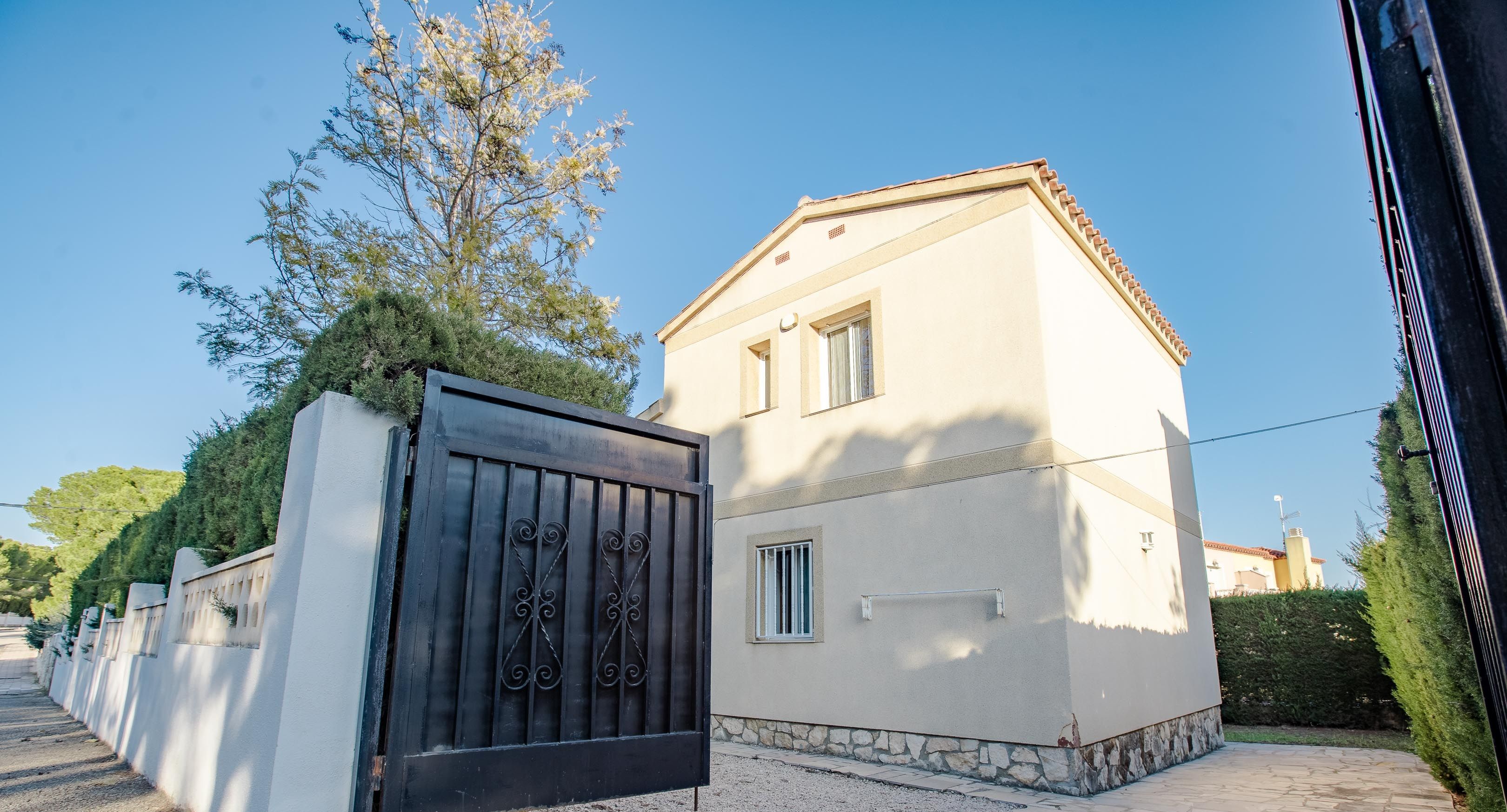 A house with a gated entrance, a stone pathway, and a clear blue sky.