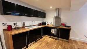 A compact kitchen with a wooden countertop, black cabinets, a stainless steel range hood, and a built-in oven. - Inviting 1-bed Apartment in Banbury (Banbury)