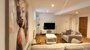 A modern living room with a large painting, a flat-screen TV, a white coffee table, and a sofa. - Inviting 1-bed Apartment in Banbury (Banbury)