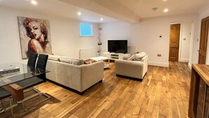 A modern living room with a flat-screen TV, two sofas, a glass dining table, and a wooden floor. - Inviting 1-bed Apartment in Banbury (Banbury)