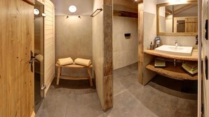 Un baño revestido de paneles de madera con un banco de madera, un lavamanos con espejo y una zona de ducha.