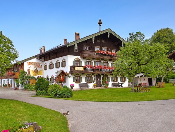 A traditional European building with a balcony adorned with flowers, a well-maintained lawn, and a clear sky.