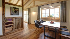 Un comedor con una mesa y sillas de madera, un banco, un estante en la pared y una ventana con cortinas.