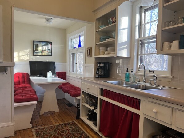 A kitchen with white cabinets, a coffee maker, a sink, and a window with a view of trees.