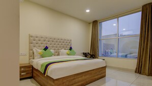 A bedroom with a large bed, a nightstand, a window with curtains, and a view of the city. - Treebo Torque (Greater Noida)