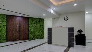 A reception area with a wooden door, a green wall, a reception desk, and a clock on the wall. - Treebo Torque (Greater Noida)