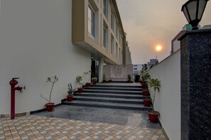 Eine Treppe führt zu einem Gebäudeeingang, der mit Blumentöpfen und einem roten Feuerlöscher versehen ist.