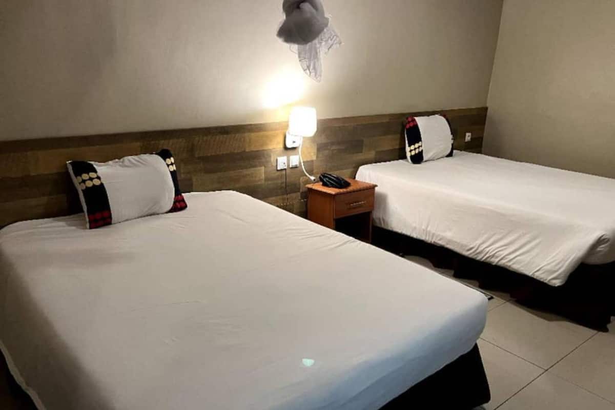 A hotel room with two beds, a nightstand with a phone, and a wall-mounted lamp.