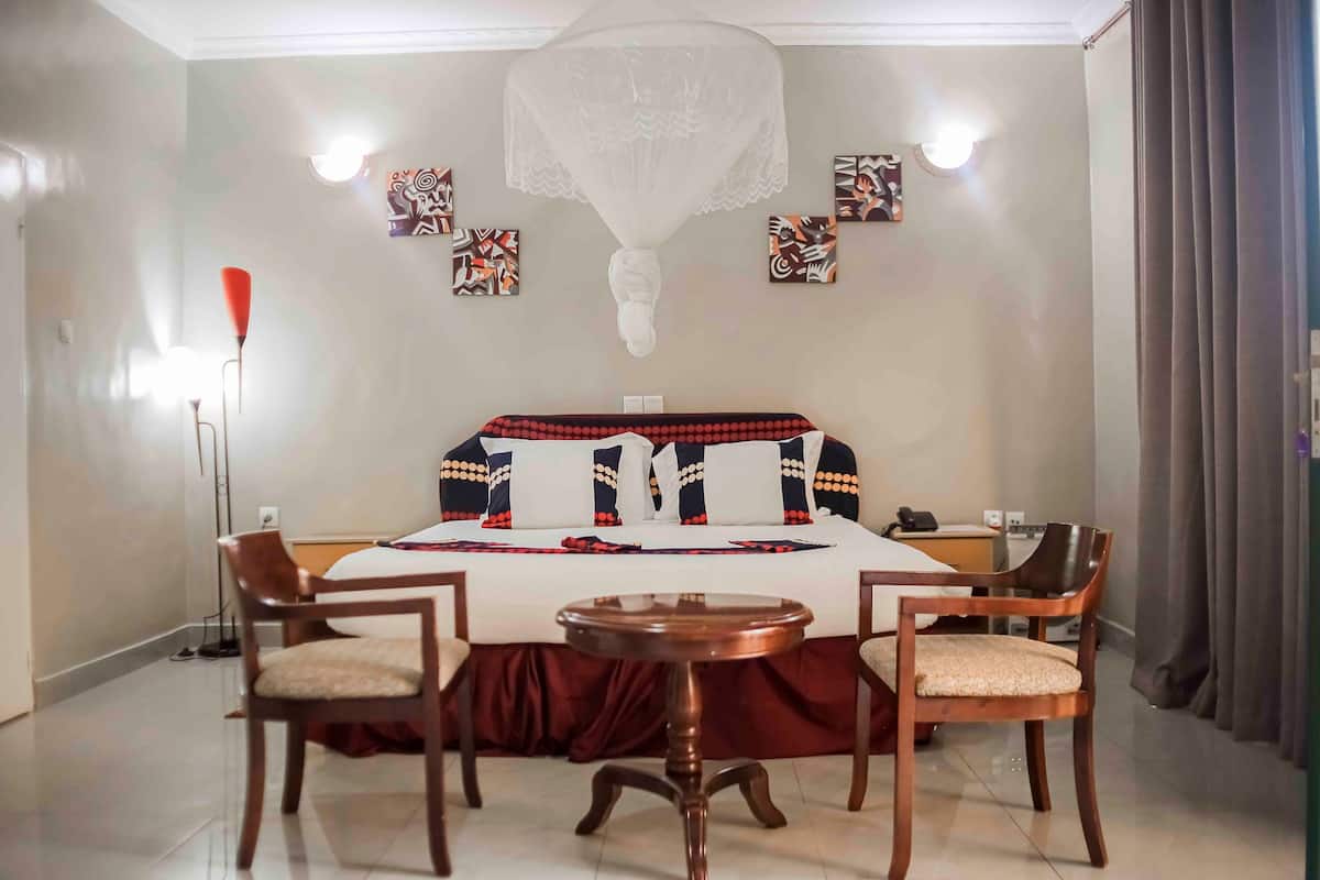 A hotel room with a large bed, two wooden chairs, a small round table, and a floor lamp.