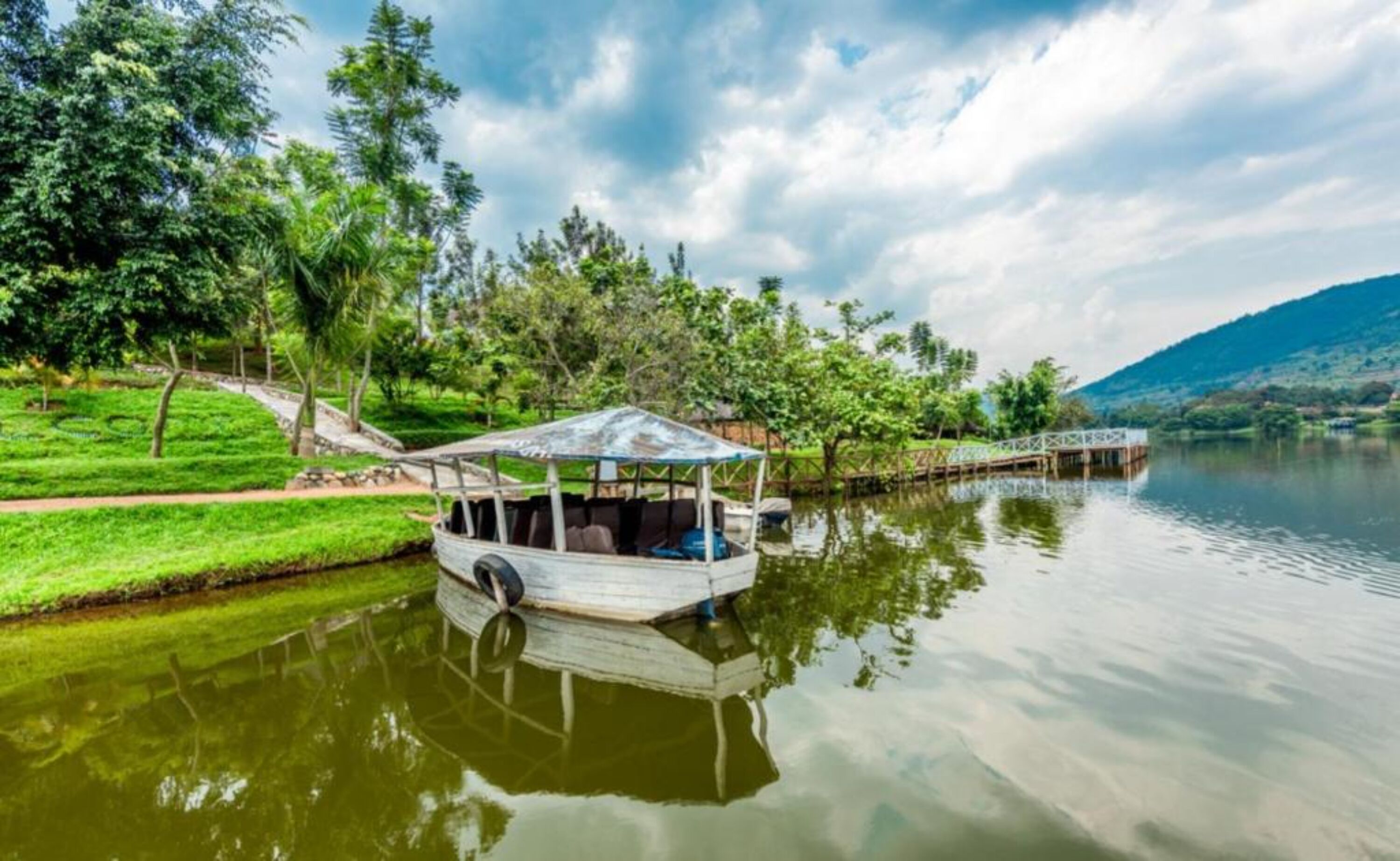 Un bateau doté d’un espace de repos abrité, naviguant sur un lac paisible, entouré d’une végétation luxuriante et d’un pont en bois.
