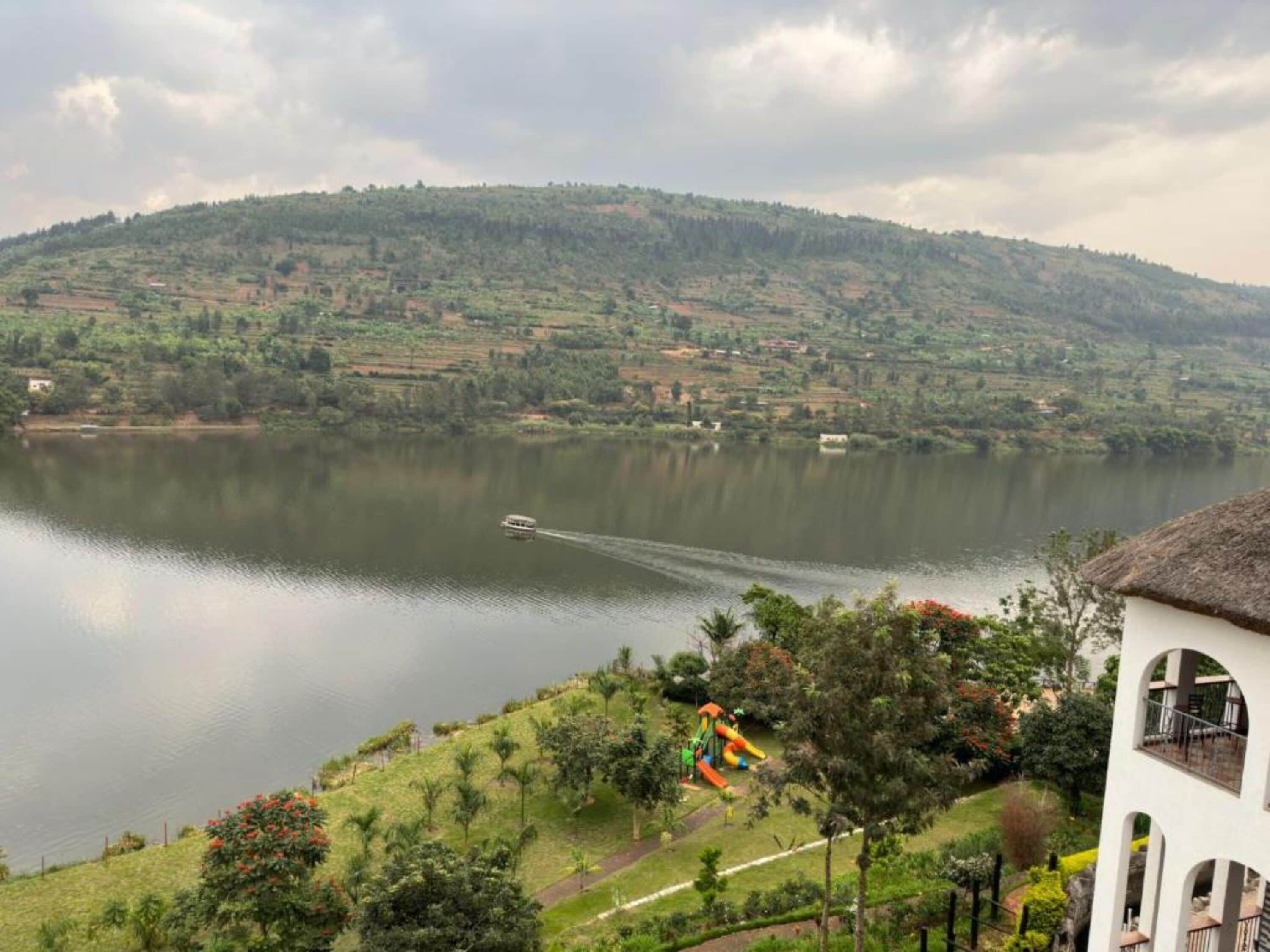 A view of a lake with a boat, surrounded by green hills and a playground.