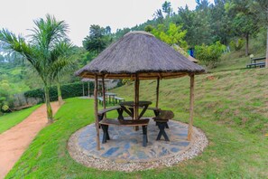 Un kiosque doté d’un toit de chaume, entouré d’une zone circulaire pavée de pierres et agrémenté de bancs.