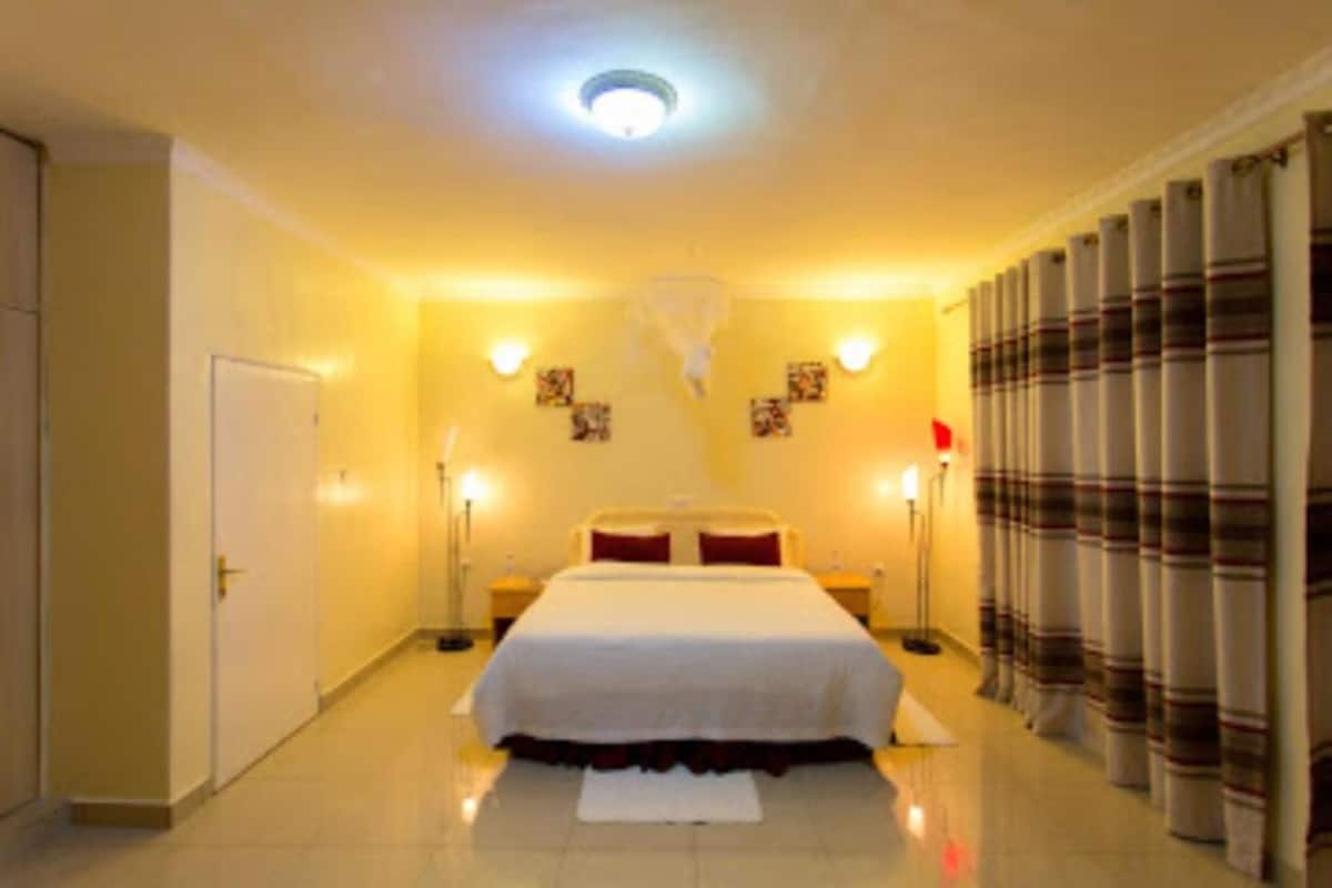 A hotel room with a large bed, bedside tables, a nightstand, a lamp, a ceiling light, and curtains.