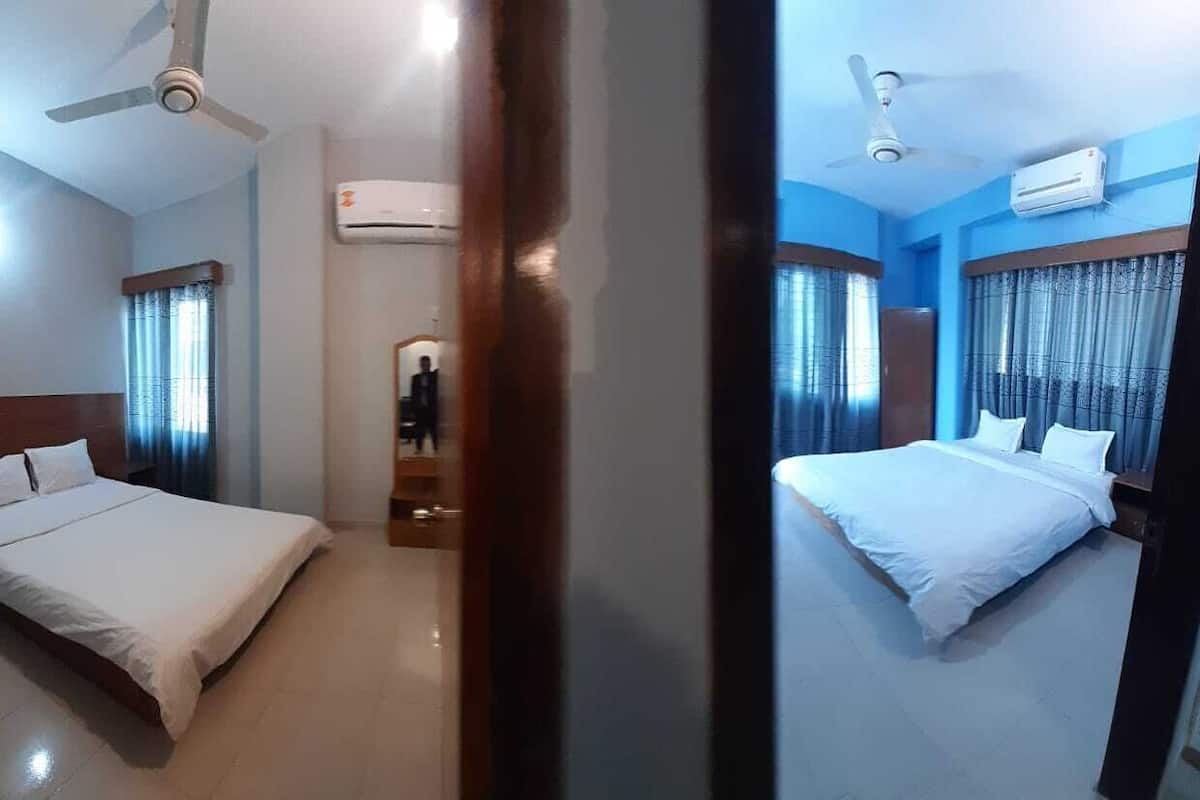 Quarto de hotel com cama, ventilador de teto, ar condicionado e vista para o corredor.