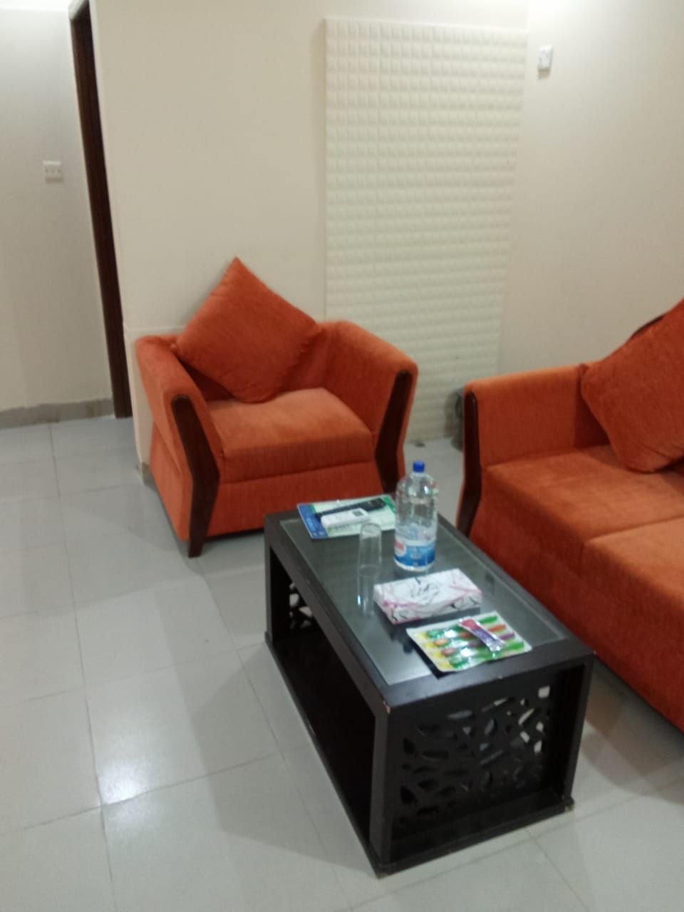A room with two orange sofas, a glass coffee table, and a tiled floor.