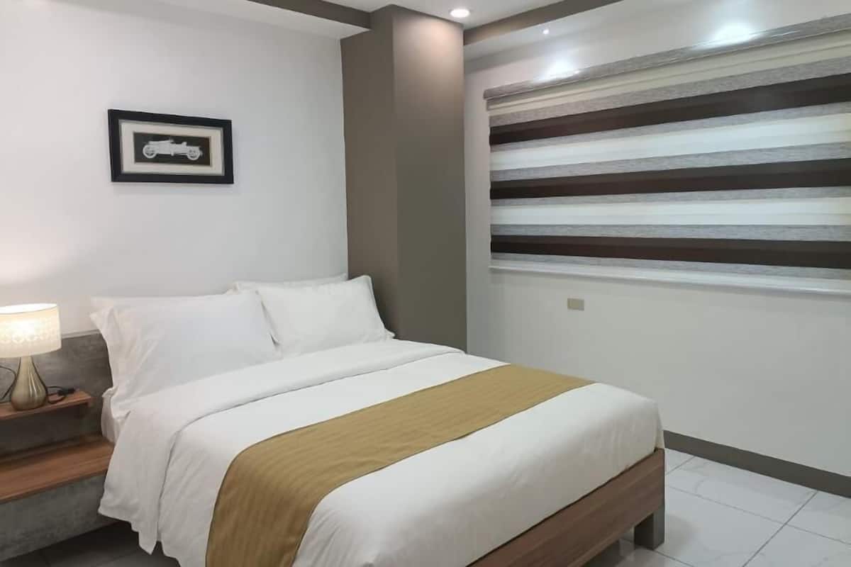 A neatly made bed with white bedding and a brown accent, a bedside table with a lamp, and a framed picture on the wall.
