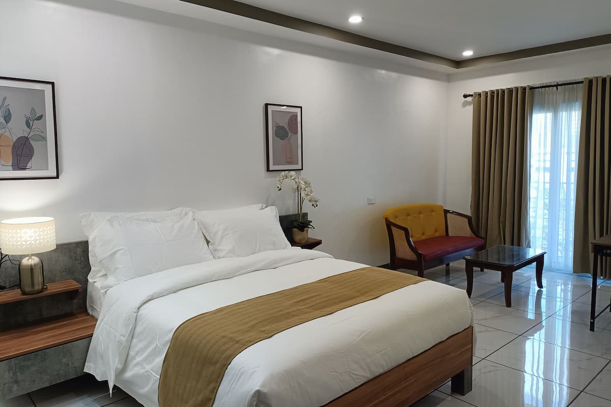 A hotel room with a bed, a chair, a table, and two framed pictures on the wall.
