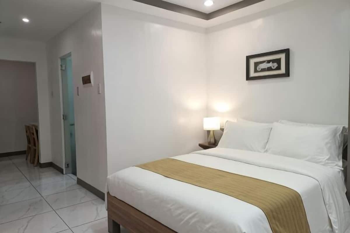A hotel room with a bed, bedside table, lamp, and a framed picture on the wall.