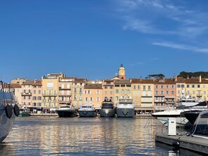A marina with boats docked, a clear sky, and buildings with a uniform architectural style in the background.