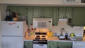 A kitchen with green cabinets, a white refrigerator, a microwave, a stove, and a sink. - Lakeside, fishing, Cozy 2/2 - 5 minutes from Branson attractions and Table Rock (Branson)