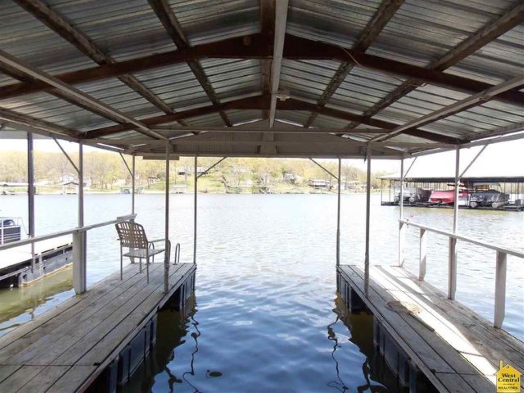 A covered dock with benches, a view of the water, and a distant bridge.
