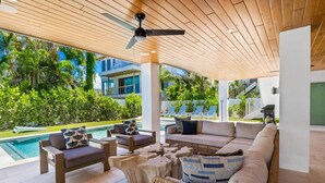 Un espace extérieur abrité avec des sièges, une piscine, des chaises longues et un ventilateur de plafond.