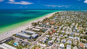Vue aérienne d’une zone résidentielle côtière, avec une plage, des maisons et quelques bâtiments commerciaux.