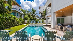 Une piscine dotée de chaises longues et d’un espace patio, le tout entouré de verdure et de bâtiments modernes.