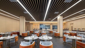 A spacious dining area with round tables and orange chairs, featuring a modern ceiling design and a view of the kitchen in the background. - Days Hotel BY Wyndham Hengyang Nanyue (Hengyang)