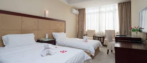 A hotel room with two beds, a desk, a chair, and a TV.