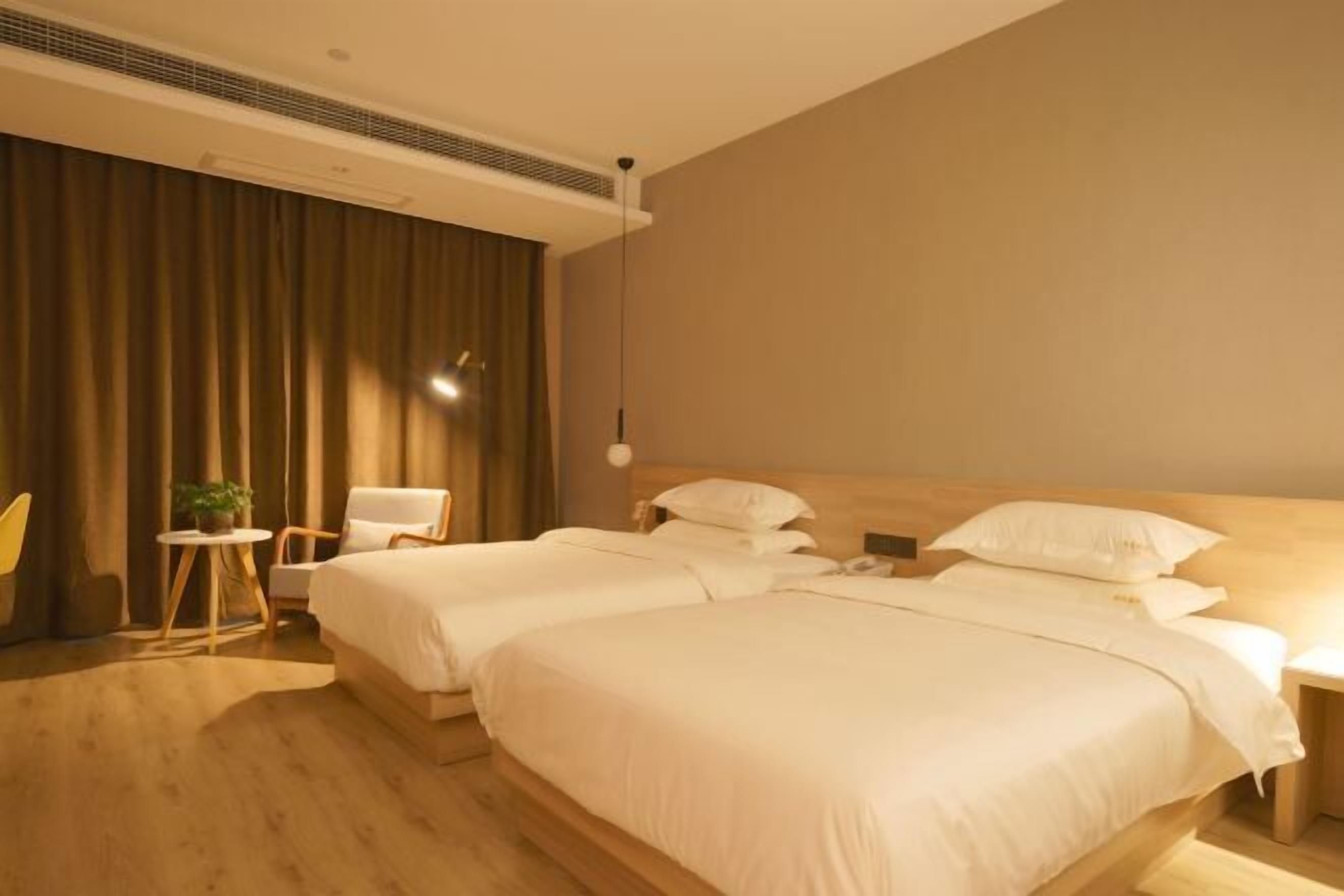 A hotel room with two beds, a small table with a plant, a chair, and a wooden floor.