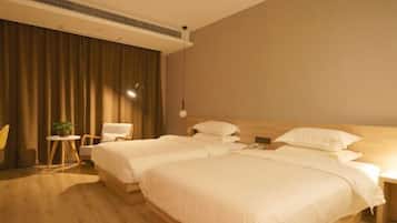 A hotel room with two beds, a small table with a plant, a chair, and a wooden floor.