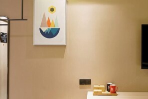 A hotel room with a framed abstract artwork, a small table with a tray, a red mug, and a television mounted on the wall. - Manring Hotel (Lijiang)