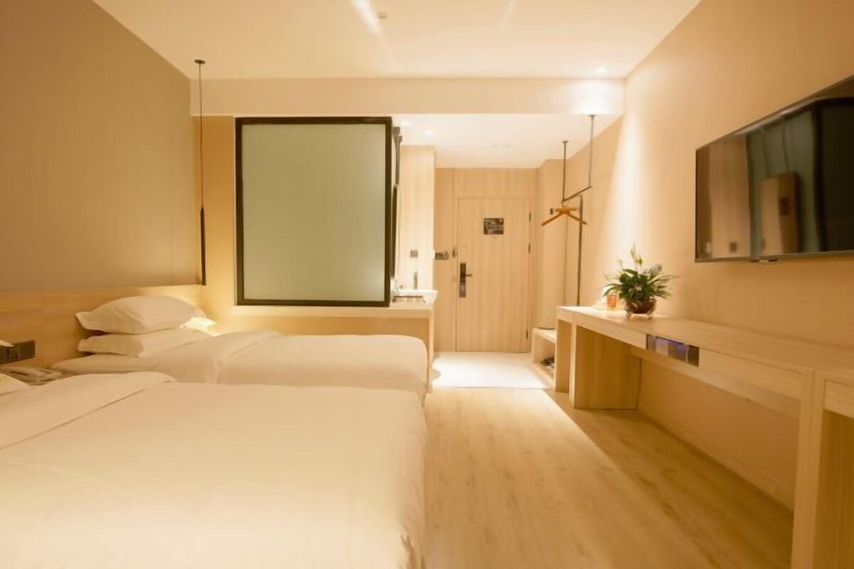 A hotel room with two beds, a wooden floor, a large mirror, a TV, and a small plant.