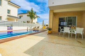 Uma área de piscina com espreguiçadeiras e uma mesa, rodeada por edifícios.