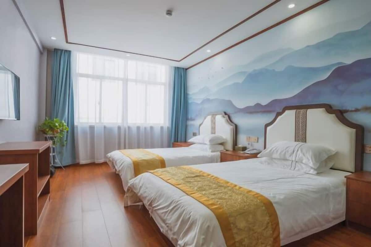 Ein Hotelzimmer mit zwei Betten, einem großen Fenster mit Vorhängen, einem Bergpanorama und Holzboden.