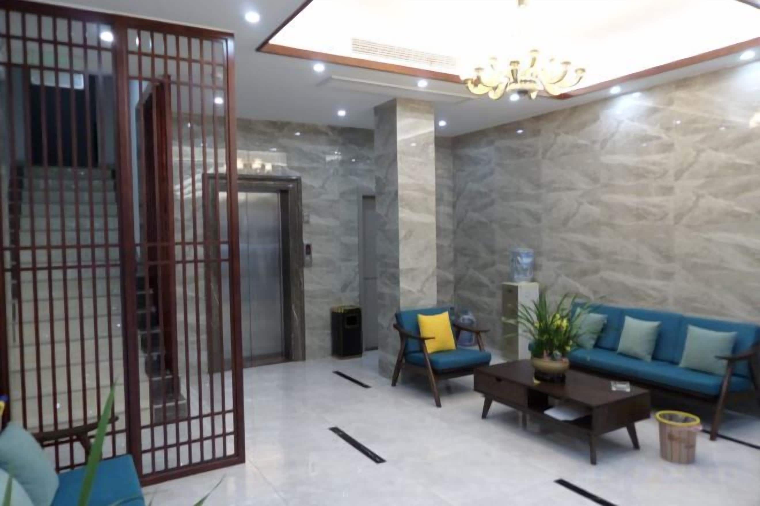 A modern lobby with a marble wall, a blue sofa, a coffee table, and a decorative plant.