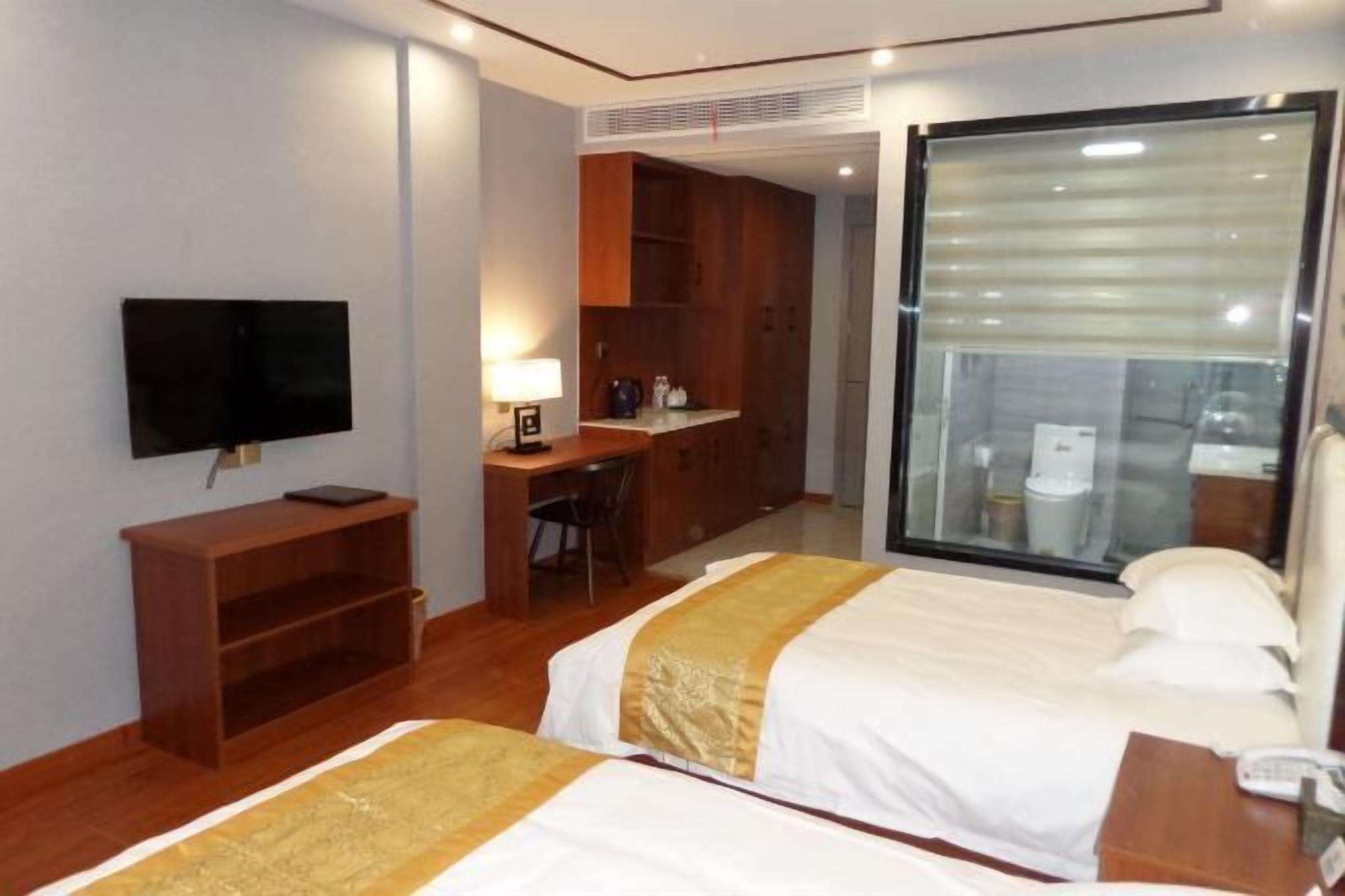 Habitación de hotel con dos camas, un escritorio, televisor y un ventanal amplio.