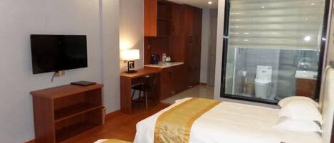 Habitación de hotel con dos camas, un escritorio, televisor y un ventanal amplio.