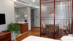 A modern hotel room with a wooden floor, a bed, a desk, a chair, a dining table with chairs, a plant, and a TV mounted on the wall. - Shangpin Business Hotel (Guangde)