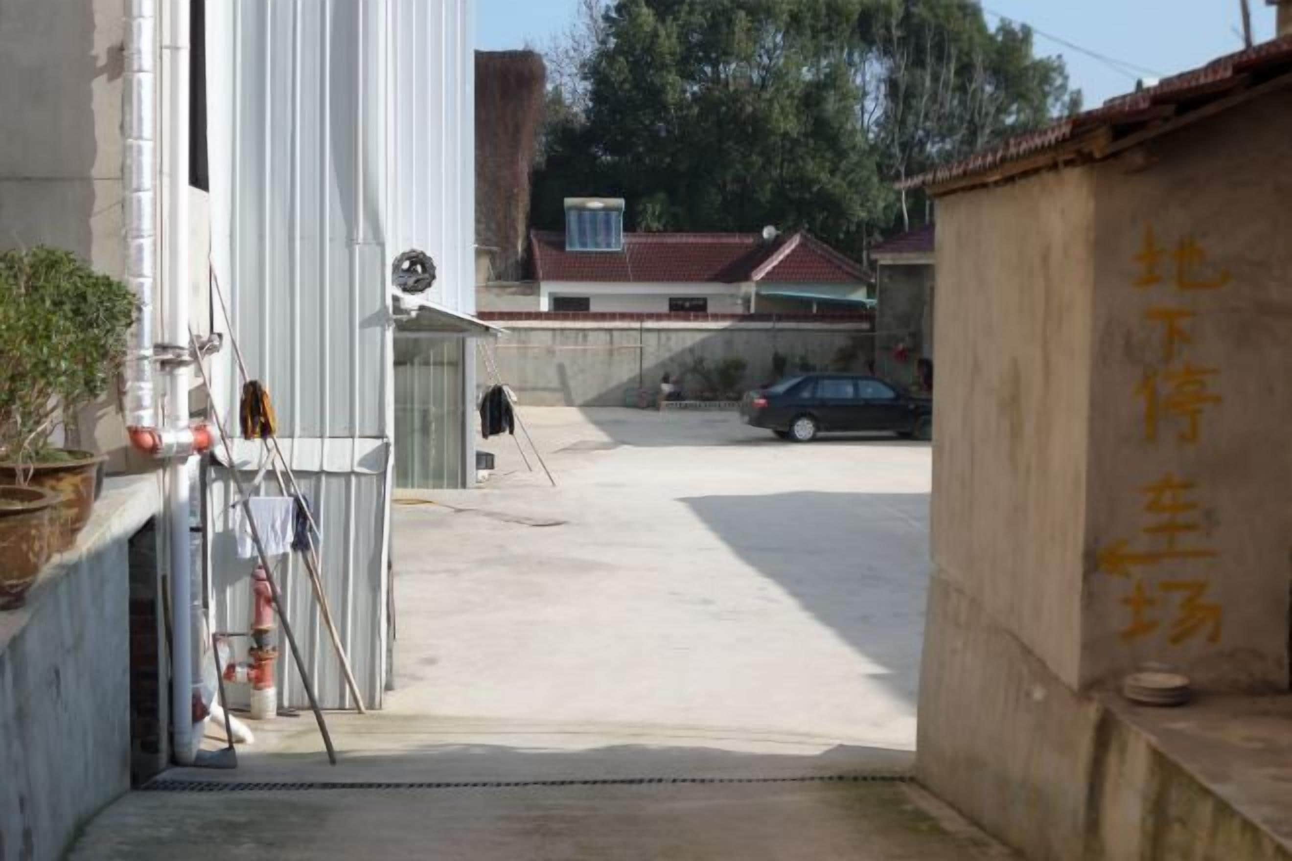 A narrow alleyway with a concrete floor, a white building on the left, and a beige wall with yellow text on the right.